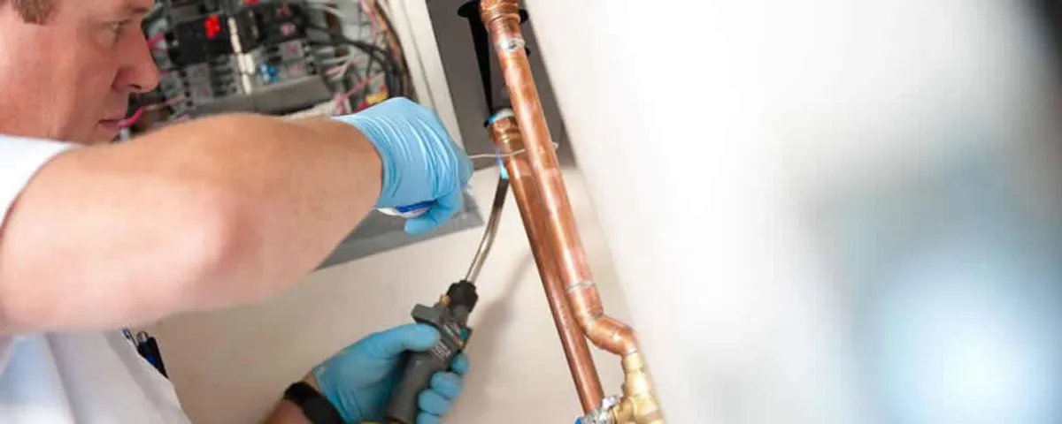 Water heater repair technician testing copper pipe connections and controls in Greensboro, NC